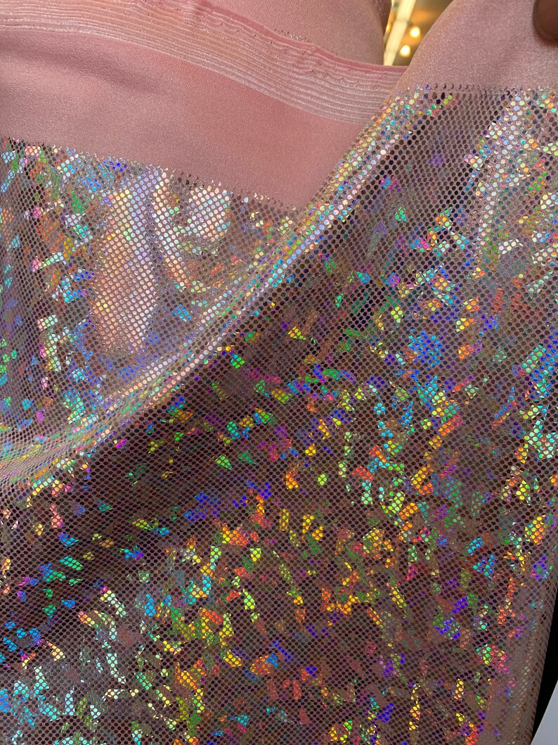 May include: A close-up of iridescent pink fabric with a textured, grid-like pattern. The fabric has a holographic finish that shimmers with rainbow colors.