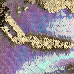 May include: Close-up of iridescent purple, blue, and white sequins with a gold sequin stripe.