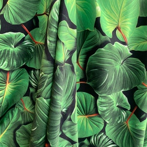 May include: Green tropical leaf fabric with a black background. The fabric has a repeating pattern of large, green leaves.