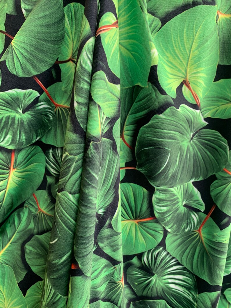 May include: Green tropical leaf fabric with a black background. The fabric has a repeating pattern of large, green leaves.