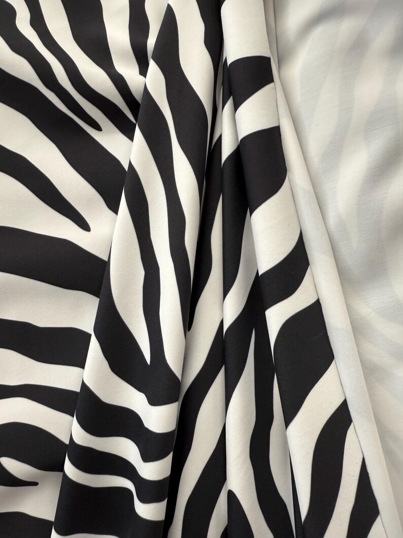 May include: Black and white zebra print fabric. The fabric is folded and shows the pattern from different angles.