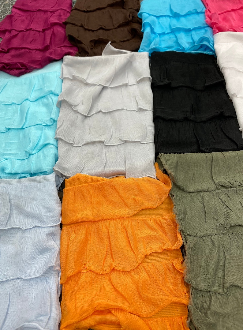 K&ouml;nnte beinhalten: Eine Sammlung von zehn Stoffstreifen mit gekr&auml;uselten Kanten in verschiedenen Farben, darunter hellblau, wei&szlig;, orange, gr&uuml;n, schwarz, braun, rosa und lila. Die Stoffstreifen sind in einem vertikalen Stapel angeordnet.