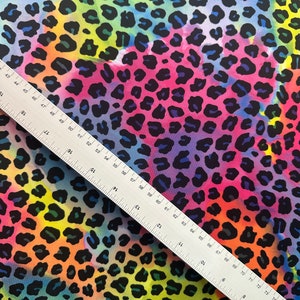 May include: A colorful fabric with a leopard print pattern. The fabric is a mix of pink, blue, yellow, and green colors. The leopard spots are black and outlined in a darker shade of blue.