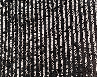 Lentejuelas negras brillantes sobre tela elástica de terciopelo negro. Diseños de rayas y lentejuelas. La tela se vende cortada a medida, de 60 pulgadas de ancho. Es elástica solo en dos direcciones.