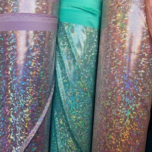 May include: Three rolls of iridescent fabric in lavender, teal, and pink. The fabric has a holographic finish with a subtle sparkle.