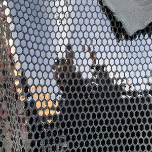 Puede incluir: Tela negra con un patrón hexagonal de lentejuelas plateadas. La tela es brillante y reflectante.