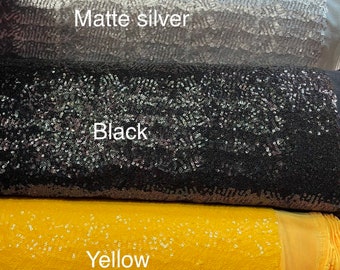 Op de afbeelding: Vijf rollen met paillettenstof in verschillende kleuren: rood, zilver, zwart, geel en paars.
