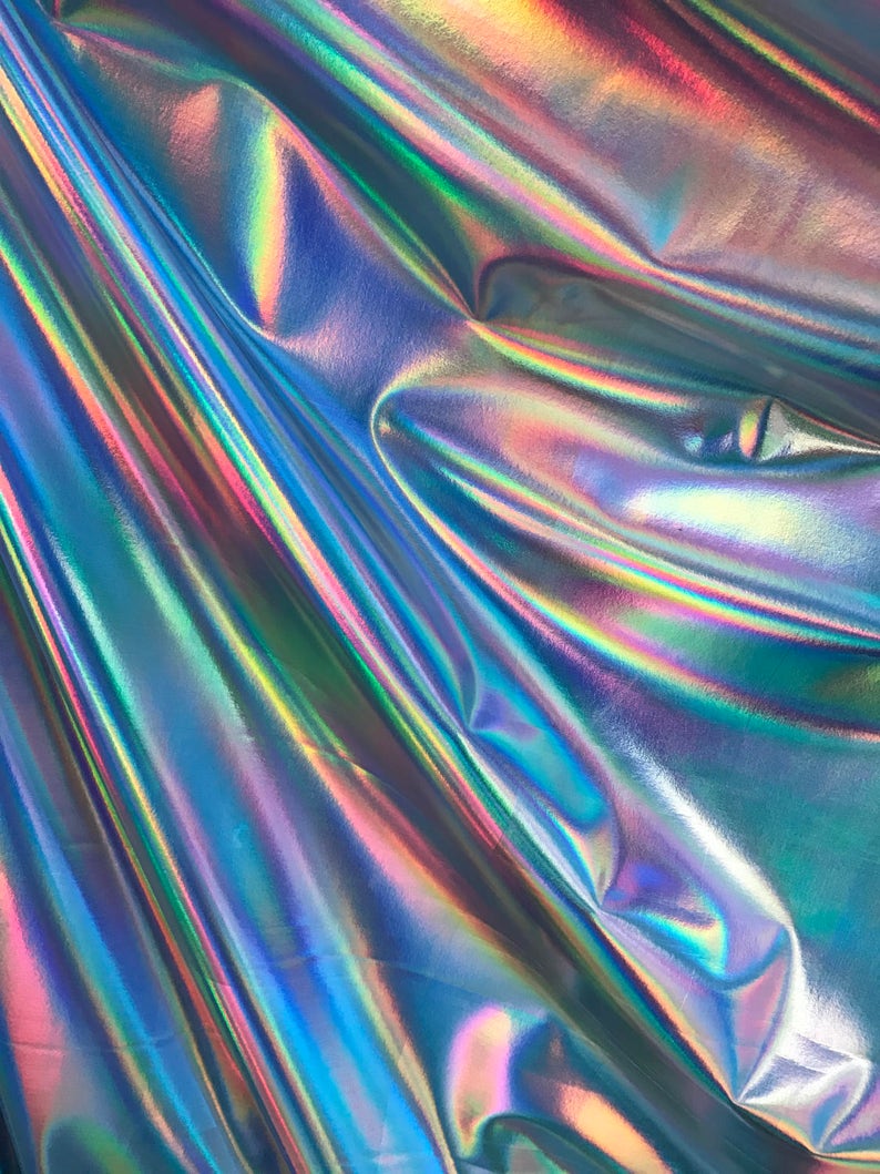 May include: A close-up of iridescent fabric with a holographic finish. The fabric is folded and draped, creating a textured and shimmering effect.