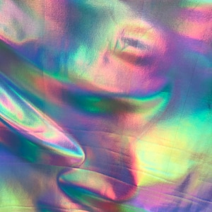 May include: A close-up of iridescent fabric with a holographic finish. The fabric is folded and has a rainbow of colours, including blue, green, pink, and purple.