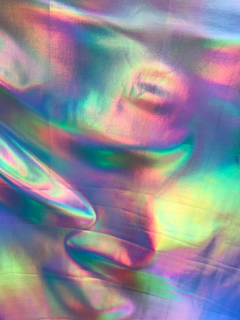 May include: A close-up of iridescent fabric with a holographic finish. The fabric is folded and has a rainbow of colours, including blue, green, pink, and purple.