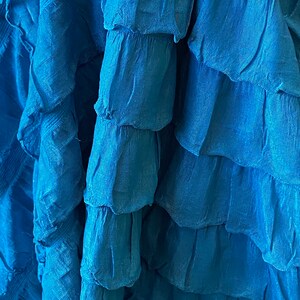 K&ouml;nnte beinhalten: Nahaufnahme eines blauen Faltenrocks. Der Stoff ist weich und flie&szlig;end, mit mehreren Lagen Falten.