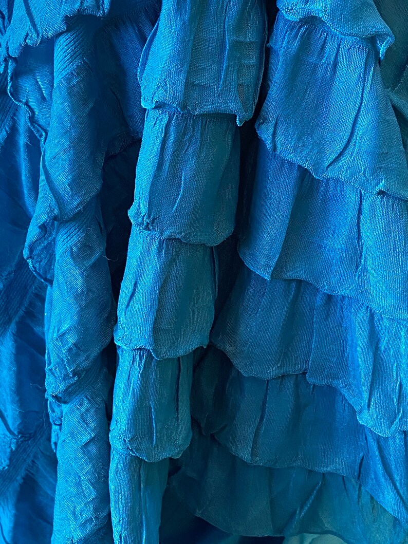 K&ouml;nnte beinhalten: Nahaufnahme eines blauen Faltenrocks. Der Stoff ist weich und flie&szlig;end, mit mehreren Lagen Falten.