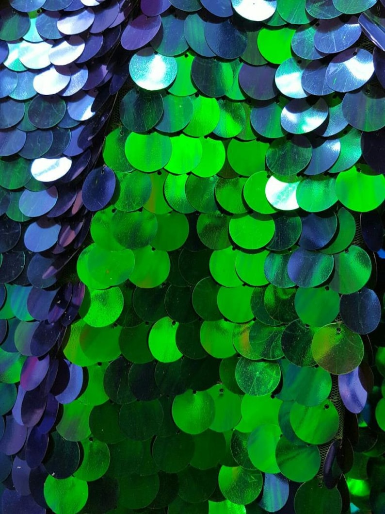 May include: Green and blue iridescent sequins arranged in a pattern. The sequins are round and have a shiny finish.