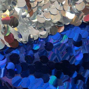 May include: A fabric with silver and blue iridescent sequins. The sequins are arranged in a pattern of overlapping circles.