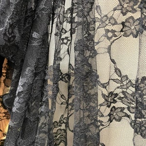 May include: Black lace fabric with a delicate floral pattern. The lace is sheer and has a soft, flowing texture.