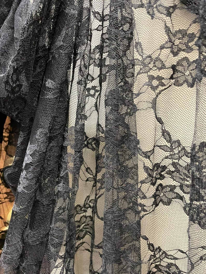May include: Black lace fabric with a delicate floral pattern. The lace is sheer and has a soft, flowing texture.