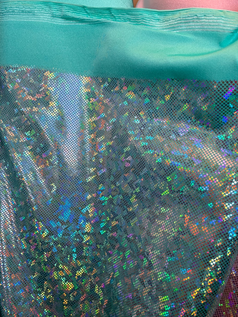 May include: Teal iridescent fabric with a small, repeating pattern of iridescent dots. The fabric has a slight sheen and is semi-transparent.
