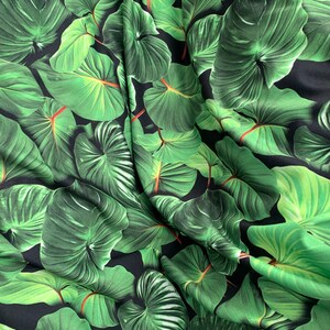 May include: Green tropical leaf print fabric with a black background. The fabric is wrinkled and has a silky texture.