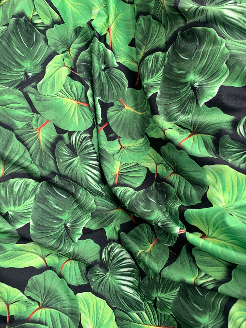 May include: Green tropical leaf print fabric with a black background. The fabric is wrinkled and has a silky texture.