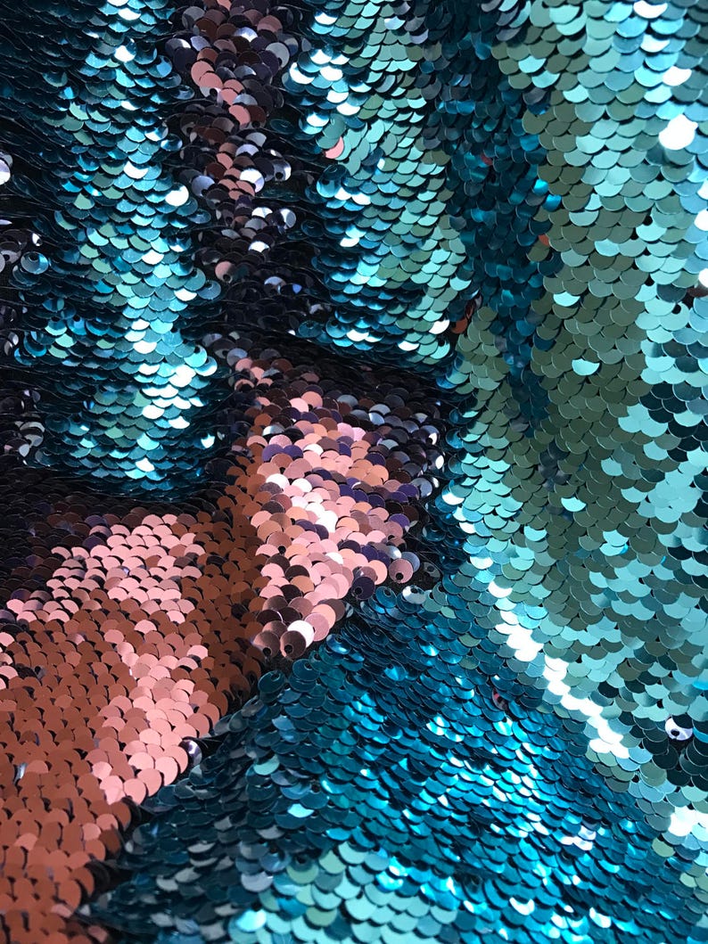 Puede incluir: Primer plano de una tela con lentejuelas turquesas y cobrizas. Las lentejuelas son redondas y se superponen, creando un efecto brillante. La tela parece ser de dos tonos, con &aacute;reas turquesas y cobrizas. La textura es suave y reflectante.