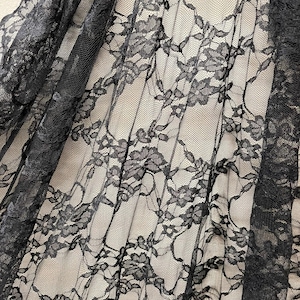 May include: Black lace fabric with a floral pattern. The lace is delicate and sheer, with a soft, flowing texture.