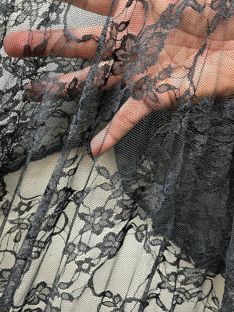 May include: Black lace fabric with a delicate floral pattern. The fabric is sheer and has a soft, flowing texture.