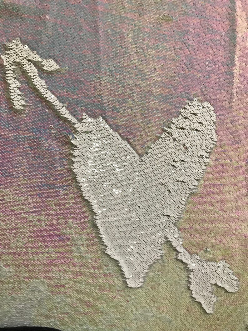 May include: A white heart with an arrow through it, made of iridescent sequins on a pink and blue background.