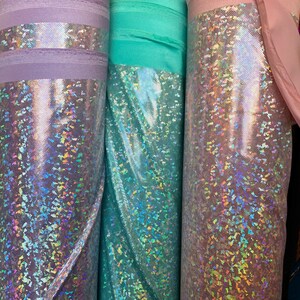May include: Three rolls of iridescent fabric in lavender, teal, and pink. The fabric has a shimmery, holographic finish.