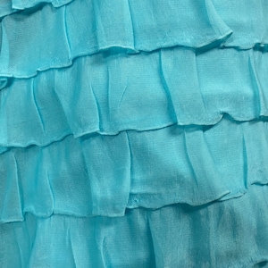 K&ouml;nnte beinhalten: Nahaufnahme eines hellblauen Stoffes mit mehreren R&uuml;schenlagen. Der Stoff hat eine weiche, flie&szlig;ende Textur.