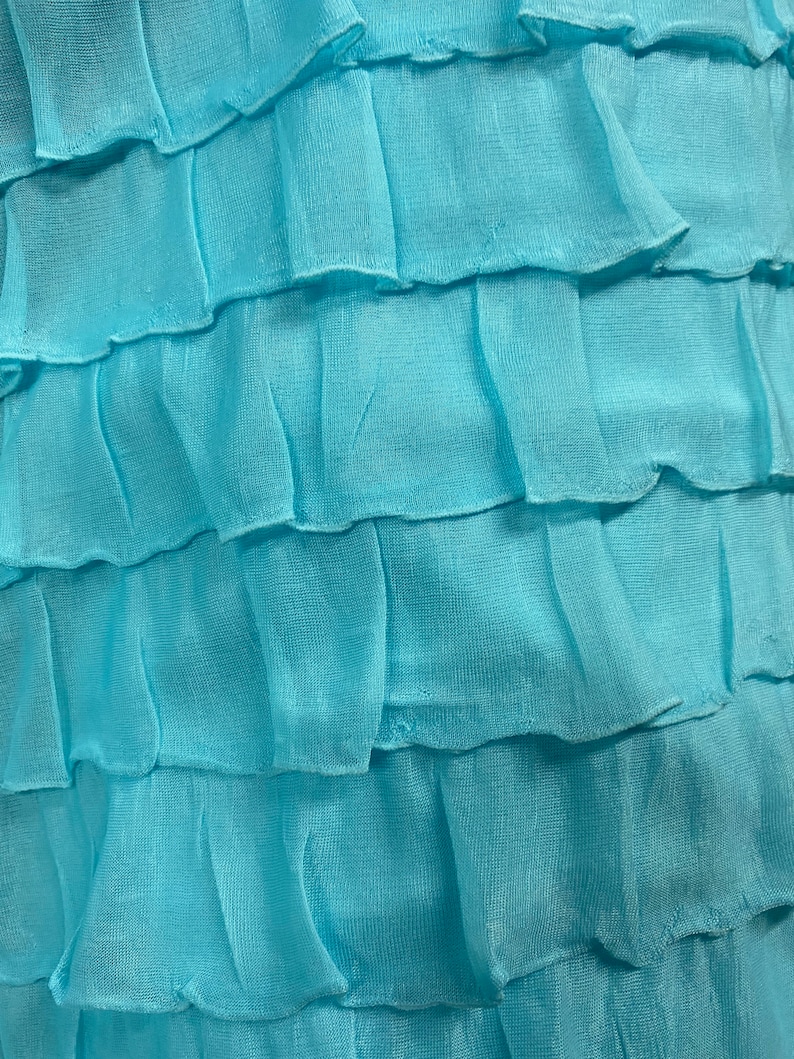 K&ouml;nnte beinhalten: Nahaufnahme eines hellblauen Stoffes mit mehreren R&uuml;schenlagen. Der Stoff hat eine weiche, flie&szlig;ende Textur.