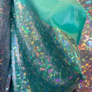May include: Teal iridescent fabric with a holographic finish. The fabric has a subtle texture and a shimmery, sparkly appearance.