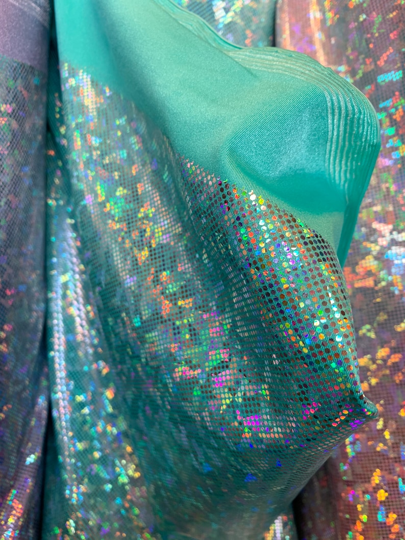 May include: Teal iridescent fabric with a holographic finish. The fabric has a subtle texture and a shimmery, sparkly appearance.