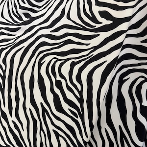 May include: Black and white zebra print fabric. The fabric has a smooth, silky texture.