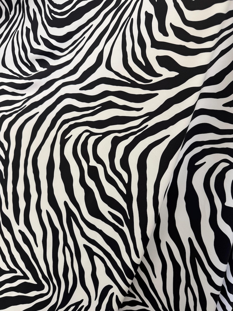 May include: Black and white zebra print fabric. The fabric has a smooth, silky texture.