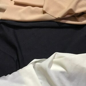 May include: Three fabric swatches in different colors: beige, black, and white. The fabric is smooth and has a slight sheen.