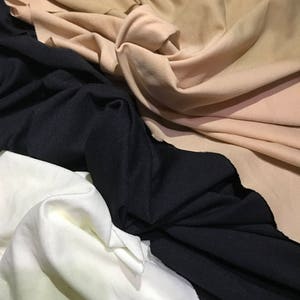 May include: Three fabric swatches in different colors: beige, black, and white. The fabric is soft and has a smooth texture.