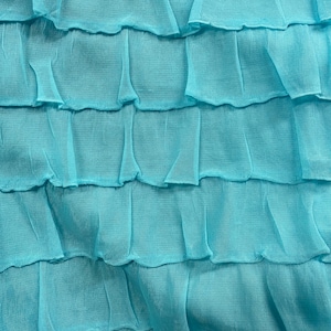 K&ouml;nnte beinhalten: Nahaufnahme eines t&uuml;rkisfarbenen Stoffes mit einer ger&uuml;schten Textur. Der Stoff ist weich und flie&szlig;end, mit einem zarten, geschichteten Design.