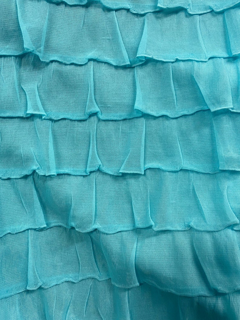 K&ouml;nnte beinhalten: Nahaufnahme eines t&uuml;rkisfarbenen Stoffes mit einer ger&uuml;schten Textur. Der Stoff ist weich und flie&szlig;end, mit einem zarten, geschichteten Design.