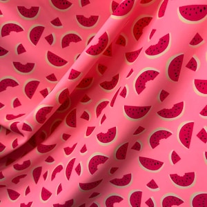 May include: Pink fabric with a repeating pattern of watermelon slices. The watermelon slices are red with black seeds and a white rind.