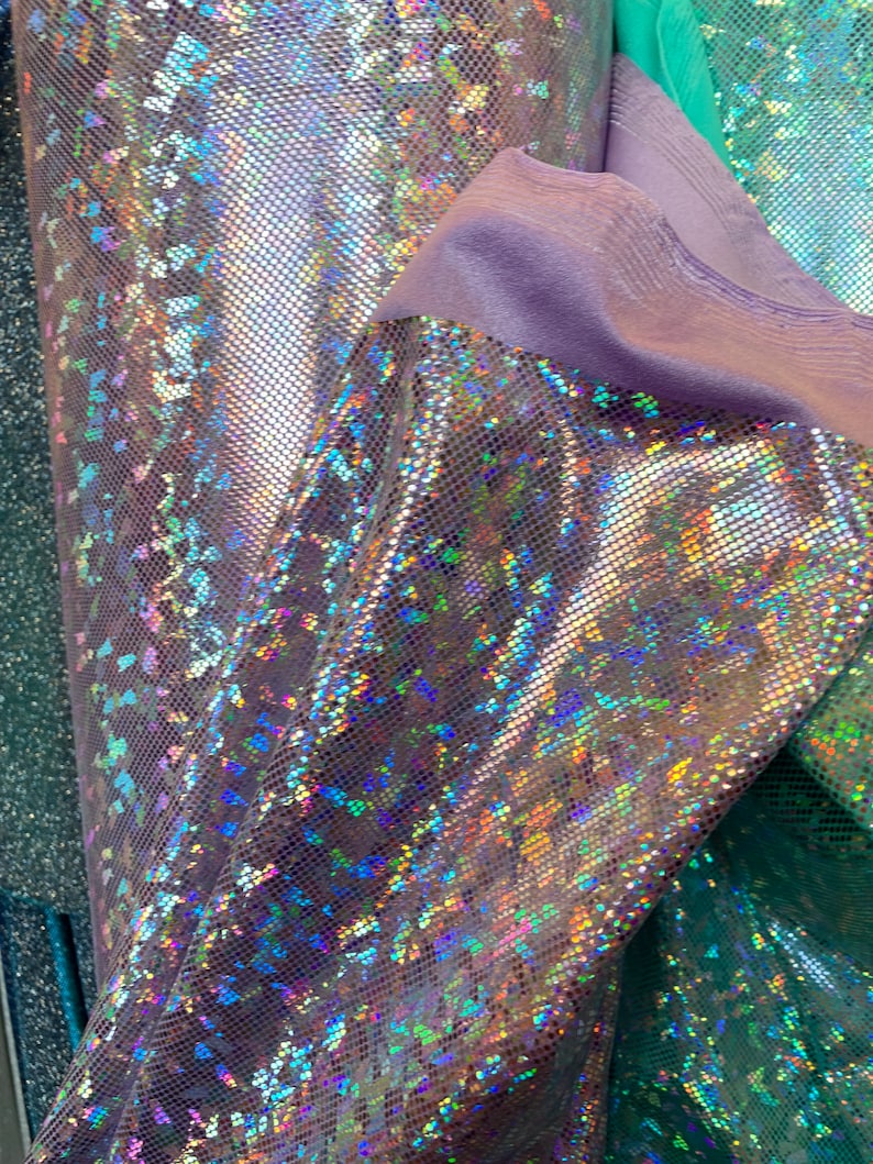 May include: Close-up of iridescent fabric with a textured, grid-like pattern. The fabric has a holographic finish with shades of blue, green, and purple.