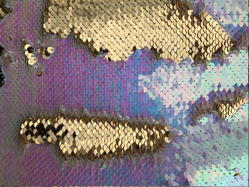 May include: Close-up of iridescent purple, blue, and white sequins with gold sequins in the background.