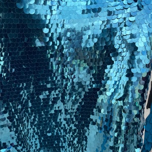 May include: Teal blue fabric with a shimmering, iridescent finish. The fabric is covered in small, overlapping sequins that create a scaly, fish-like pattern.