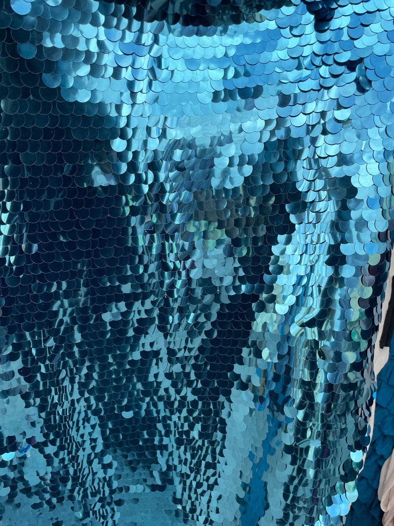 May include: Teal blue fabric with a shimmering, iridescent finish. The fabric is covered in small, overlapping sequins that create a scaly, fish-like pattern.