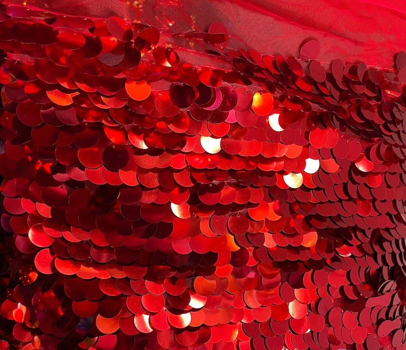 May include: Red sequin fabric with a shiny finish. The sequins are arranged in a scale-like pattern.