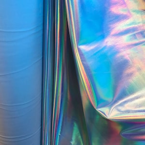 May include: Close-up of iridescent fabric with a blue and purple sheen. The fabric is folded and draped over a roll of light blue fabric.