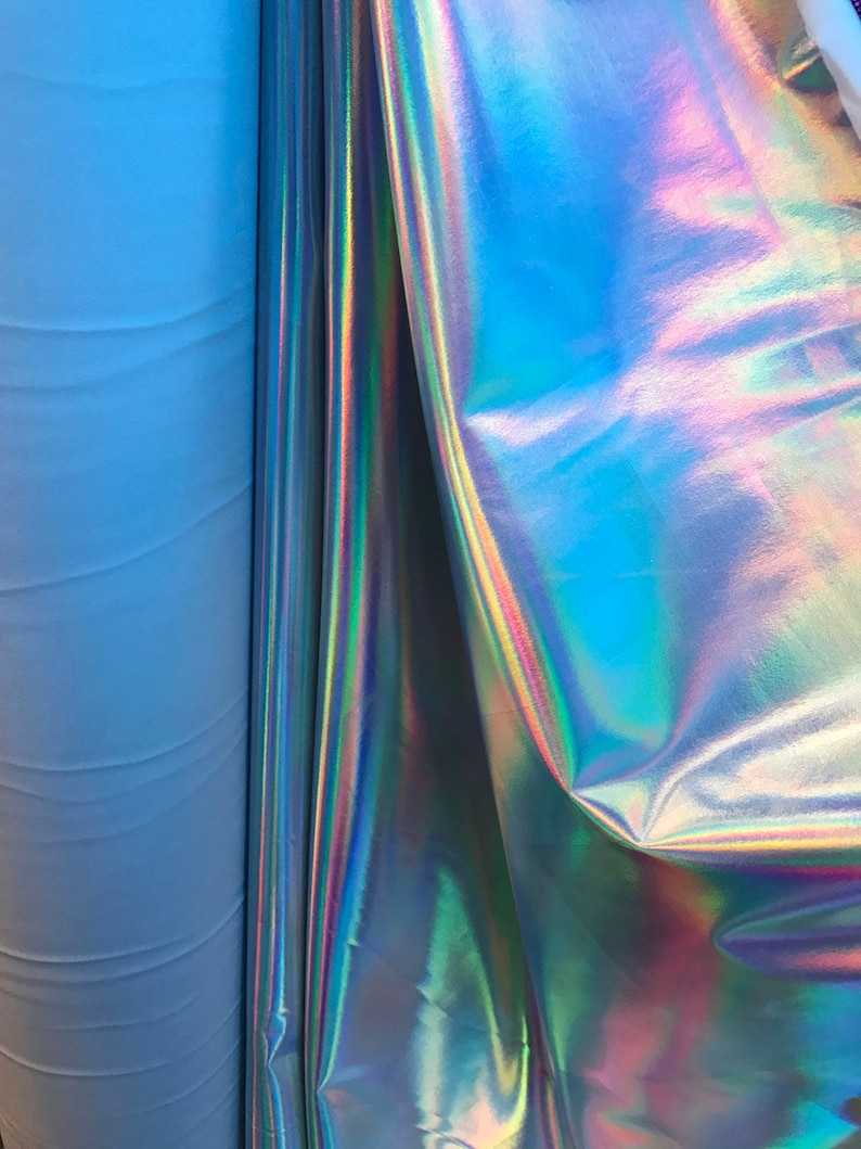 May include: Close-up of iridescent fabric with a blue and purple sheen. The fabric is folded and draped over a roll of light blue fabric.
