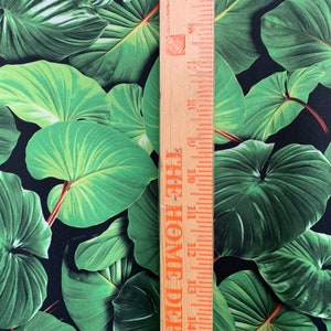 May include: Close-up of a black fabric with a green tropical leaf print. A wooden ruler with the text "THE HOME DEPOT" is placed next to the fabric.