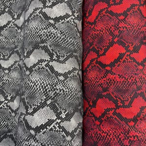 May include: Close-up of fabric rolls with a snakeskin pattern. One roll has a grey and black design, the other a vibrant red and black pattern. The fabric has a textured appearance.