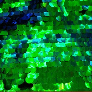 May include: Green and blue iridescent sequins arranged in a scale pattern. A wooden ruler with inch markings is visible at the bottom of the image.