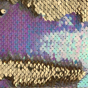 May include: Close-up of iridescent sequins in shades of purple, blue, and gold. The sequins are arranged in a pattern of overlapping scales.